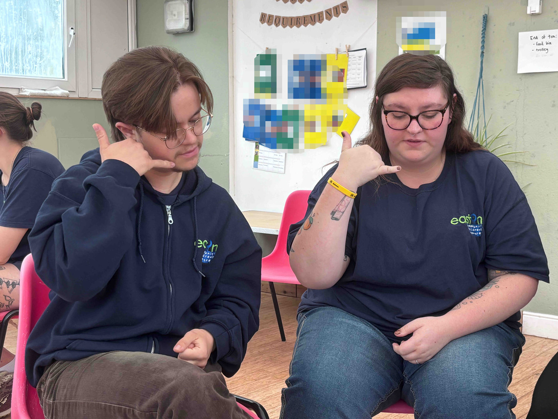 Two participants sitting together and practising Makaton signs during a small-group activity.